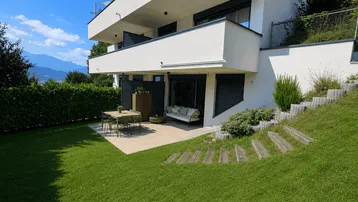 Moderne Wohnanlage mit großer Rasenfläche, gepflegtem Garten und sonniger Terrasse mit Bergblick.