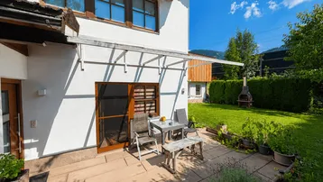 Sonnige Terrasse mit Gartenmöbeln, angrenzendem Rasen und Grillplatz im Freien.