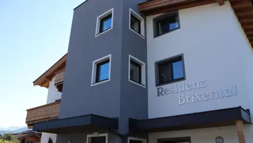 Modernes Gebäude mit grauer und weißer Fassade, Holzbalkonen und klarem Himmel.