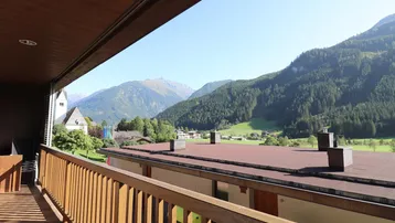 Geräumiger Balkon mit Holzboden und Geländer, bietet einen weiten Blick auf die umliegende Berglandschaft.