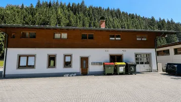 Gebäude mit weißer Fassade, Holzverkleidung und Blick auf den bewaldeten Berg.