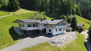 Wohnhaus in sonniger Hanglage mit Blick auf die umliegende Berglandschaft und Wälder.