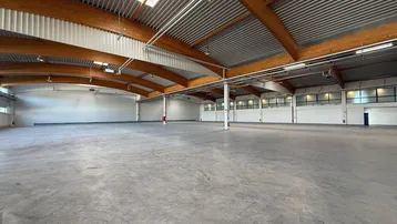 Weitläufige Lagerhalle mit hohen Decken, sichtbaren Holzträgern und Oberlichtern, bietet viel Tageslicht.
