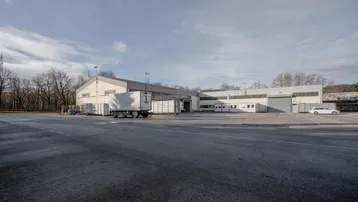 Großes Gewerbegebäude mit weitläufigem Vorplatz und Parkmöglichkeiten unter bewölktem Himmel.