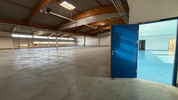 Geräumige Lagerhalle mit offenem blauen Tor, das zu einem weiteren hellen Raum führt, mit Betonboden.