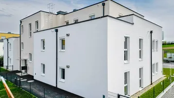 Modernes Mehrfamilienhaus mit weißer Fassade und vielen Fenstern unter blauem Himmel.