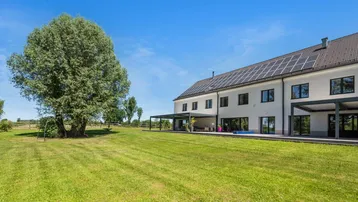 Großzügige Rasenfläche neben dem Haus mit überdachten Terrassen und Solarpaneelen auf dem Dach.