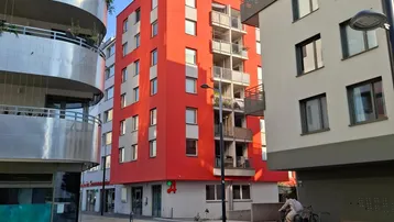 Moderne Wohngebäude mit leuchtend roter Fassade und Balkonen in einer städtischen Umgebung.