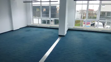 Geräumiger, leerer Büroraum mit großen Fenstern und blauem Teppichboden, bereit zur individuellen Gestaltung.