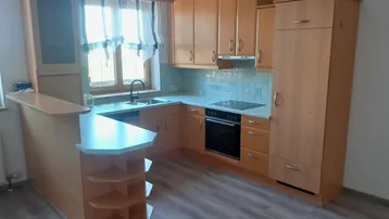 Helle Küche mit Holzschränken, integrierten Geräten, einem Frühstückstresen und Fenster über der Spüle.