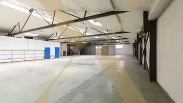 Große, leere Lagerhalle mit hohen Decken, sichtbaren Stahlträgern und Oberlichtern für Tageslicht.