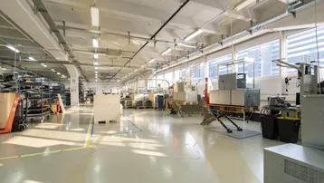 Geräumige Produktionshalle mit hohen Decken, großen Fenstern und industrieller Beleuchtung.