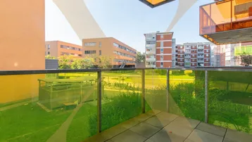 Balkon mit Glasbrüstung und Blick auf den grünen Innenhof sowie umliegende Wohngebäude.