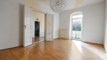 Helles Wohnzimmer mit Parkettboden, hohen Türen und Zugang zu einem französischen Balkon.