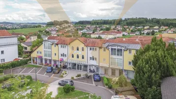 Luftaufnahme eines Wohnkomplexes mit umliegender Bebauung und grüner Landschaft unter bewölktem Himmel.