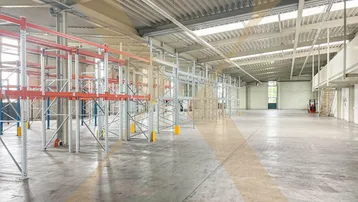 Geräumige Lagerhalle mit hohen Decken, Tageslicht und bereits installierten Regalsystemen.