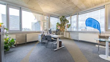 Geräumiges Büro mit großen Fenstern, Teppichboden und Blick auf die Stadt, ausgestattet mit Schreibtischen.