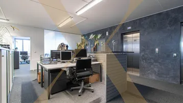 Großraumbüro mit modernen Arbeitsplätzen und Aufzugzugang, ausgestattet mit Teppichboden und funktionaler Beleuchtung.