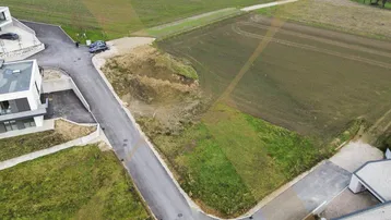 Luftaufnahme eines Baugrundstücks mit angrenzenden Feldern und modernen Gebäuden in ländlicher Umgebung.