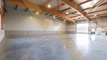Geräumige Lagerhalle mit hohen Decken, sichtbaren Holzträgern und einem robusten Betonboden, bereit zur Nutzung.