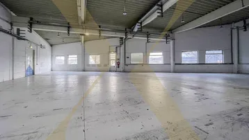 Große, leere Lagerhalle mit hohen Decken und mehreren Fenstern, ideal für industrielle Nutzung.
