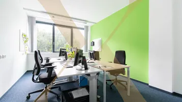 Helles und modernes Büro mit mehreren Arbeitsplätzen, grüner Akzentwand und großen Fenstern.