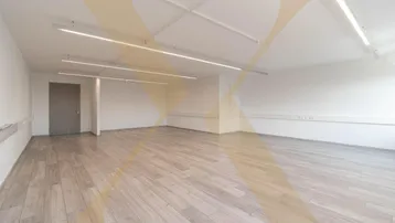 Geräumiger, leerer Büroraum mit hellem Holzboden und modernen Deckenleuchten, bereit zur individuellen Gestaltung.