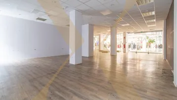 Geräumige, leere Gewerbefläche mit Säulen, abgehängter Decke und großen Schaufenstern zu einem Einkaufsbereich.