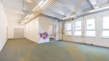 Großer, heller Gewerberaum mit Teppichboden, hohen Decken und sichtbaren Installationen, ideal für Büros oder Lager.