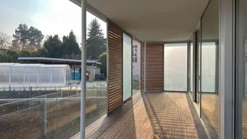 Geräumiger Balkon mit Holzdeck, Glasgeländer und weitem Blick in die Umgebung.