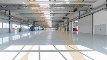Große, helle Lagerhalle mit glänzendem Boden, Oberlichtern und Kranbahn für industrielle Nutzung.