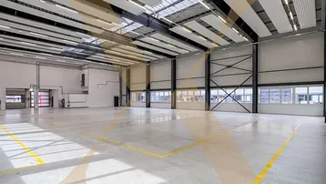 Geräumige Lagerhalle mit hoher Decke, Betonboden und Oberlichtern, ideal für industrielle Nutzung.