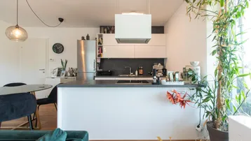 Moderne Einbauküche mit weißen Schränken, dunkler Arbeitsplatte und Kochinsel.