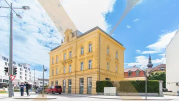 Historisches Gebäude mit gelber Fassade an einer Straßenecke unter blauem Himmel.