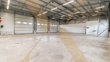 Geräumige Lagerhalle mit hohen Decken, Industrieboden und mehreren Rolltoren für den Zugang.