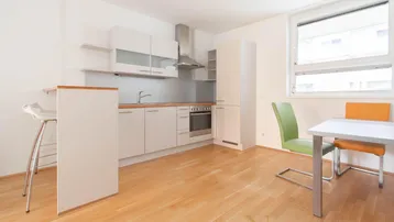 Helle, offene Küche mit weißer Einbauküche, Frühstücksbar und Essbereich mit Holzboden.