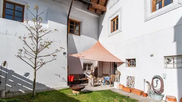 Innenhof mit Rasenfläche, kleiner Sitzecke unter einem Sonnensegel und weiß getünchten Fassaden.