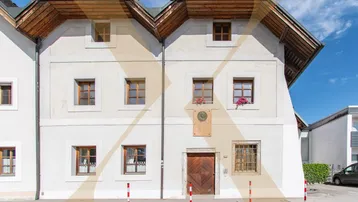 Historisches Gebäude mit weißer Fassade, Holzdach und traditionellen Fenstern unter blauem Himmel.
