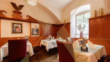 Traditioneller Gastraum mit Holztäfelung, gedeckten Tischen und einem Fenster mit Tageslicht.