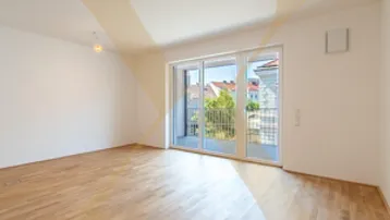 Helles, unmöbliertes Zimmer mit Holzboden und Zugang zu einem Balkon mit Stadtblick.
