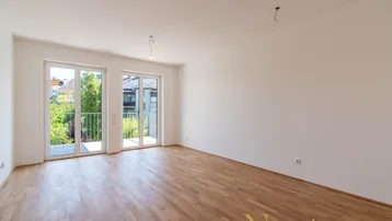 Helles, leeres Zimmer mit Parkettboden und Zugang zu einem französischen Balkon.