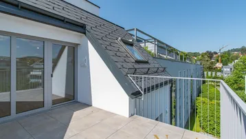Dachterrasse mit Fliesenboden und Blick auf die Umgebung, angrenzend an das moderne Gebäude.