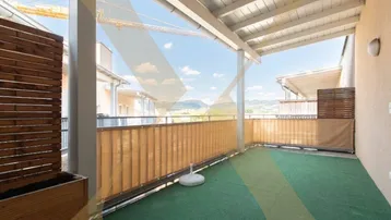 Geräumiger Balkon mit grünem Bodenbelag und weitem Blick auf die umliegende Landschaft und Berge.