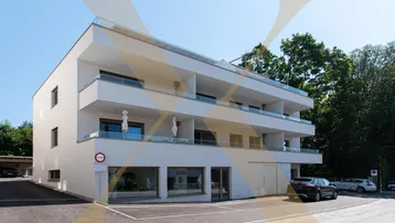 Modernes Mehrfamilienhaus mit weißer Fassade, Balkonen und Parkplätzen im Freien.