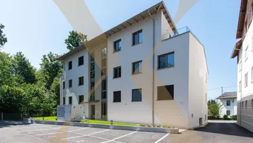 Modernes weißes Mehrfamilienhaus mit großen Fenstern, Außenjalousien und einem angrenzenden Parkplatz.