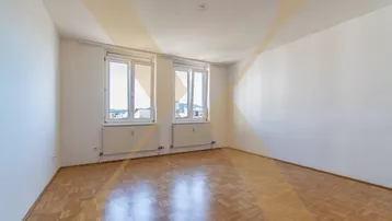 Helles, leeres Zimmer mit Parkettboden und zwei Fenstern, die einen weiten Ausblick bieten.