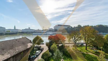 Panoramablick auf die Stadt mit Fluss, historischen Gebäuden und grünen Ufern unter blauem Himmel.