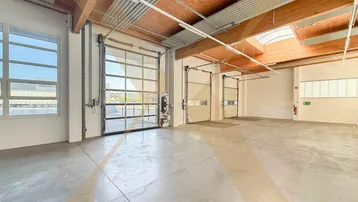 Geräumige Lagerhalle mit hohen Decken, Betonboden und mehreren Rolltoren für einfachen Zugang.