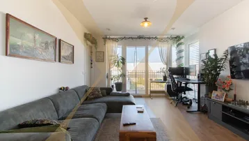 Helles Wohnzimmer mit großem Sofa, Arbeitsbereich und Zugang zum Balkon, modern eingerichtet.