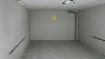 Leere Garage mit Betonboden und Wänden, ausgestattet mit Deckenbeleuchtung und Garagentoröffner.
